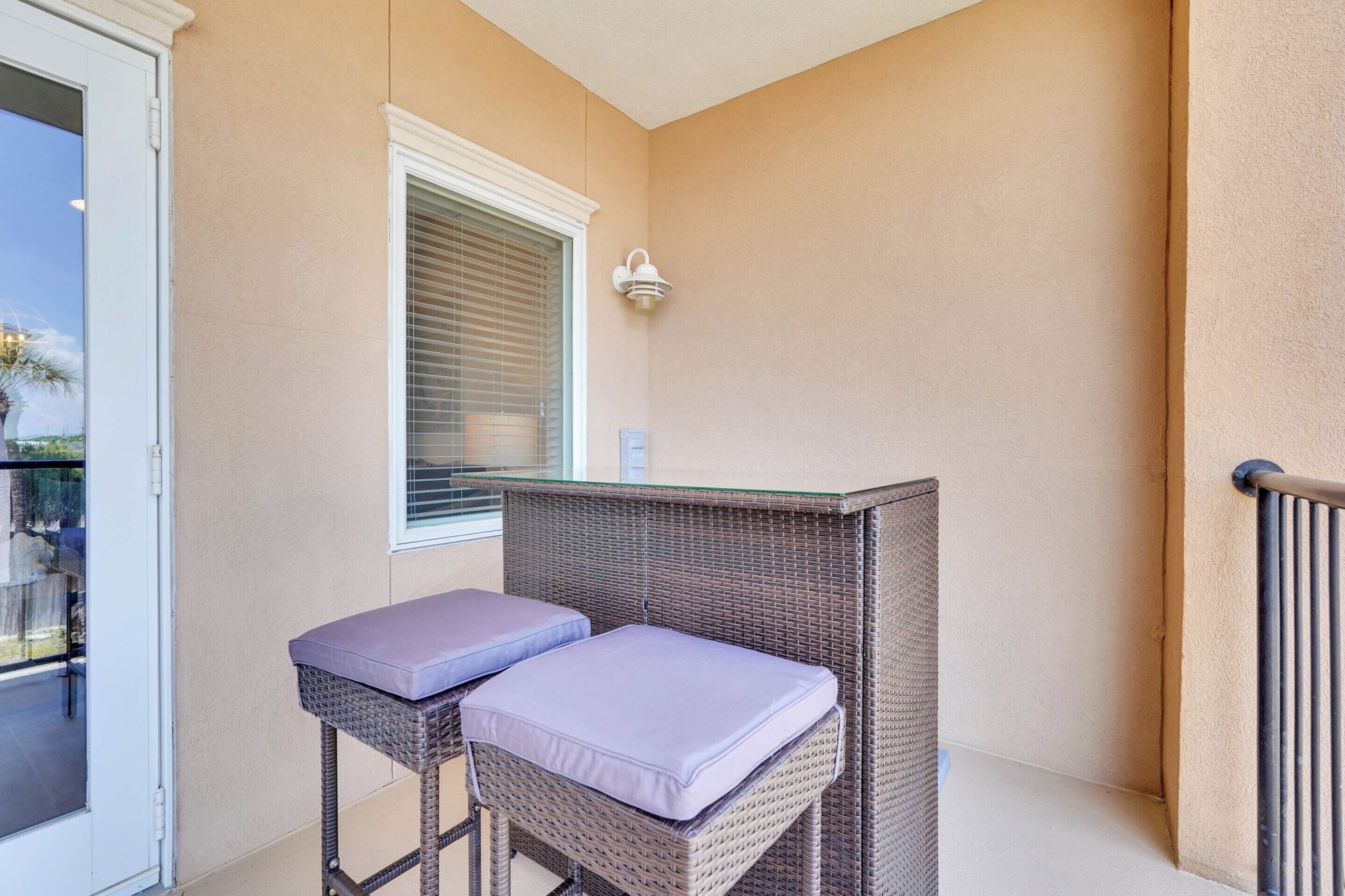Een balkon met rieten meubels, een tafel met glazen blad en een raam met zonwering.
