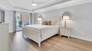 A bedroom with a bed, bedside tables, a ceiling fan, and a view of the outdoors.