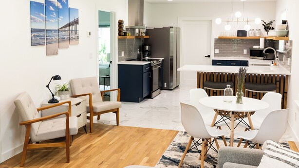 A modern kitchen with a central island, a dining area with a round table, and a living space with a sofa and chairs. - New and Modern Double En-Suite (Pensacola)