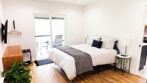 A bedroom with a large bed, bedside lamps, a wooden dresser, a potted plant, and a sliding glass door leading to a balcony. - New and Modern Double En-Suite (Pensacola)