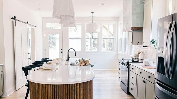 A modern kitchen with a central island, stainless steel appliances, and large windows. - The Cowboy (Southern Pines)