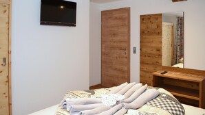 A bedroom with a bed, a wooden wardrobe, a television mounted on the wall, and a mirror above a wooden dresser. - Beautiful home in Mariapfarr with WiFi (Mariapfarr)