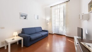 Un salon avec un canapé, une petite table avec une lampe, un téléviseur et une fenêtre avec des rideaux.
