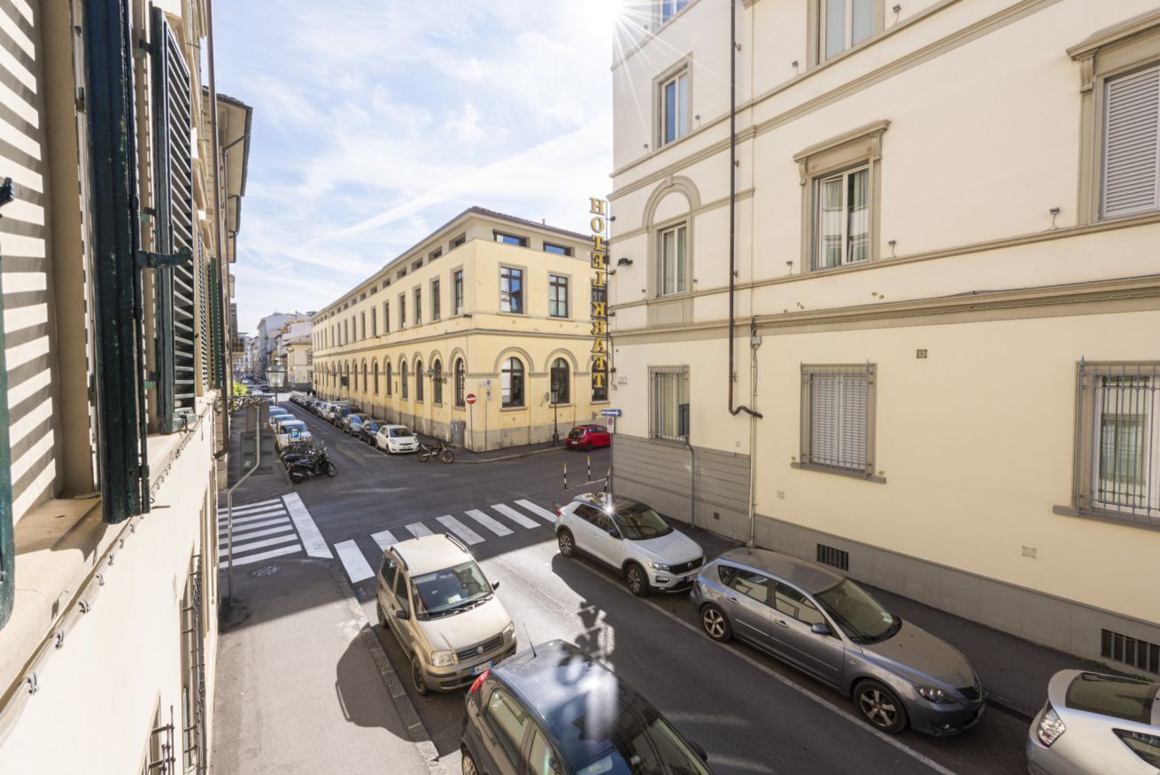 A street view with parked cars, a pedestrian crossing, and buildings with balconies.