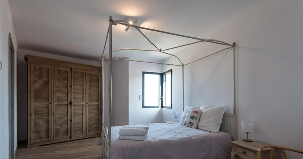 A bedroom with a four-poster bed, a wooden wardrobe, and a window providing natural light.