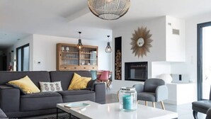 Ein modernes Wohnzimmer mit einem grauen Sofa, einem weißen Couchtisch und einem Glasgefäß. Es gibt einen Holzkasten mit Glastüren und einen dekorativen Spiegel an der Wand.