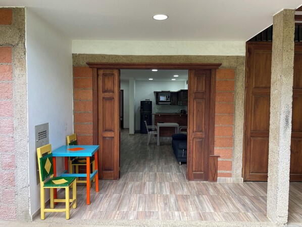 A room with a wooden door, a table with chairs, and a kitchen area in the background.