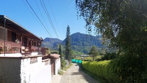 Un edificio tradicional con balcón, rodeado de abundante vegetación y montañas al fondo.