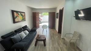 Una sala de estar moderna con un sofá negro, una mesa de centro de madera y un televisor montado en la pared.