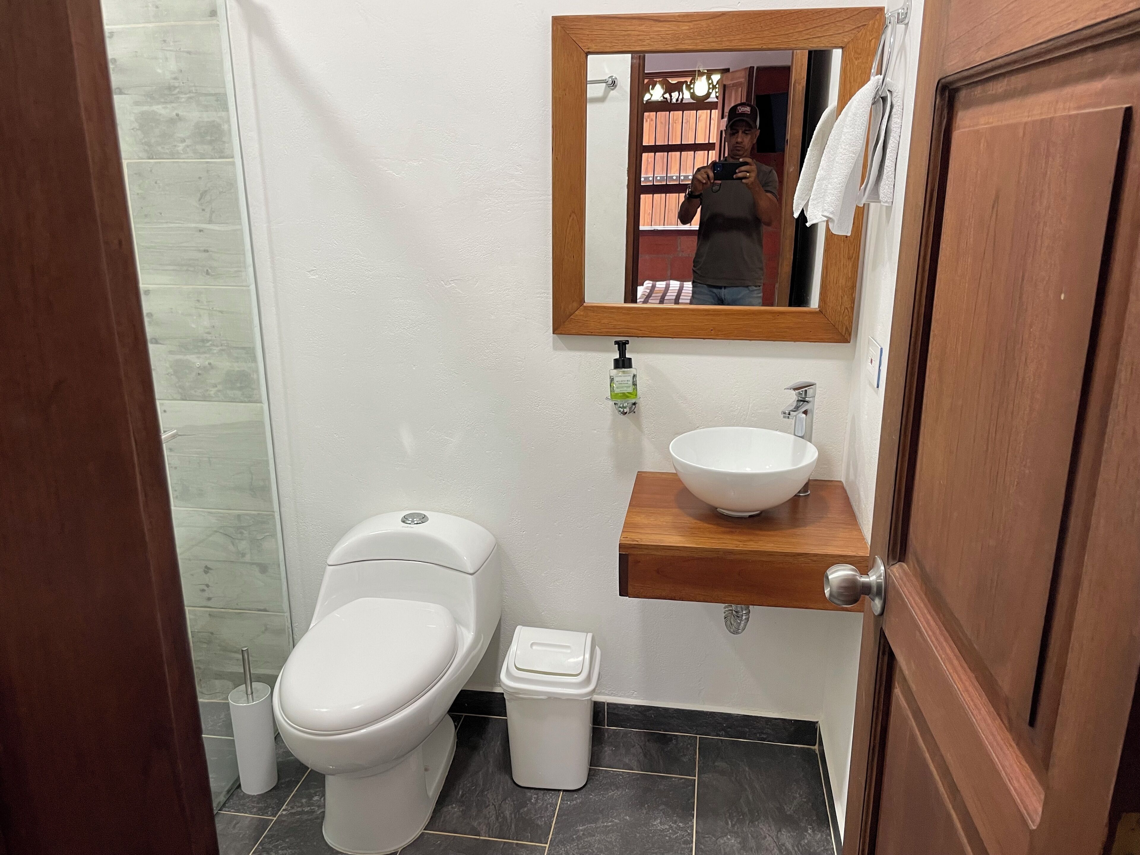 A bathroom with a white toilet, a sink with a wooden countertop, a mirror, and a small trash bin.