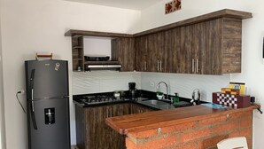 Una cocina compacta con armarios de madera oscura, un refrigerador negro, una estufa a gas y un lavamanos con grifo.