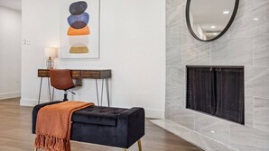 A modern living room with a black ottoman, a wooden console table, a brown leather chair, and a framed abstract painting on the wall. - Feel at Home! New Renovated House By *Grandscapes* (The Colony)