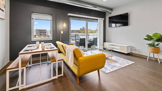 Un salon moderne avec un canapé jaune, une table à manger et une grande fenêtre donnant sur la ville.