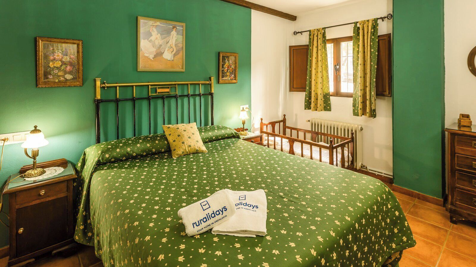 Una stanza con una coperta verde, una testiera in legno, un comodino con una lampada e una finestra con tende.