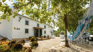 A white building with a tiled roof, potted plants, and a hammock. - Cortijo Entre Sierras Carcabuey by Ruralidays (Córdoba)