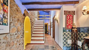 Una escala amb parets de pedra i una llinda groga, que condueix a una habitació amb un paviment de rajoles i un panell decoratiu vermell.