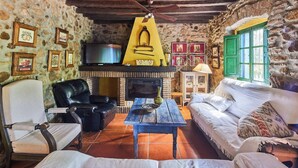 Habitació rústica amb paret de pedra, una llar de foc, un televisor, un sofà i una taula de cafè.