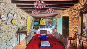 Una estada rústica amb parets de pedra, sostre de fusta, taula de dinar vermella i una cadira groga.