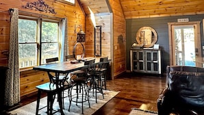 A cozy cabin interior with a dining area, a leather sofa, and a ceiling fan.