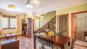 Een ruime keuken met een centraal eiland, een eethoek met een houten tafel en stoelen, en een trap naar een verdieping.