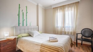 Een slaapkamer met een bed, nachtkastje, stoel en raam met gordijnen.