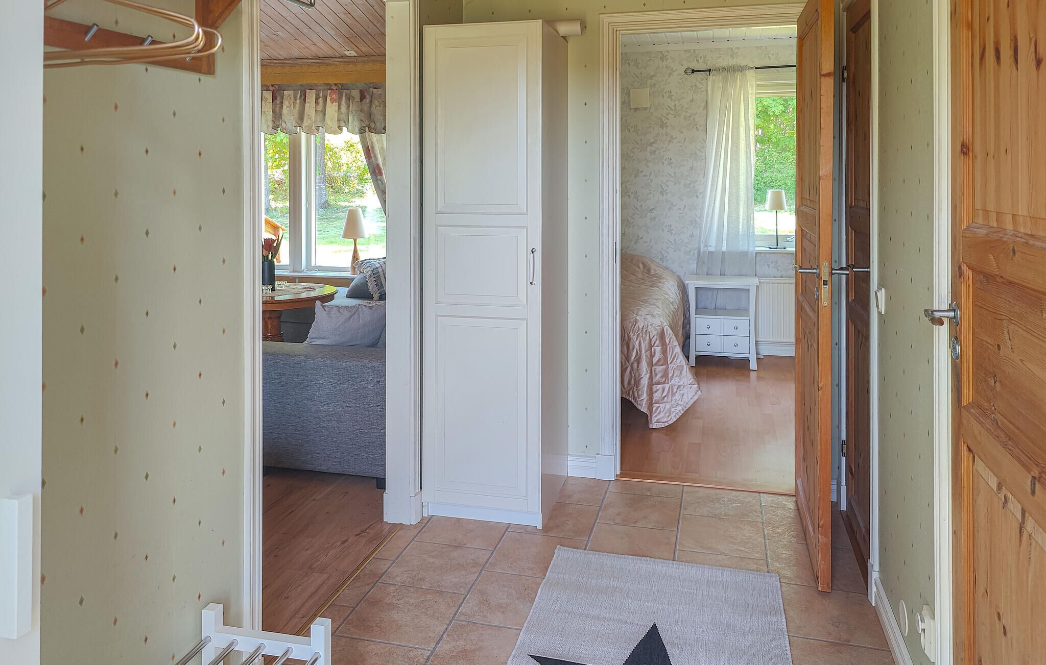 A room with a bed, a nightstand, a window with curtains, and a door leading to another room.