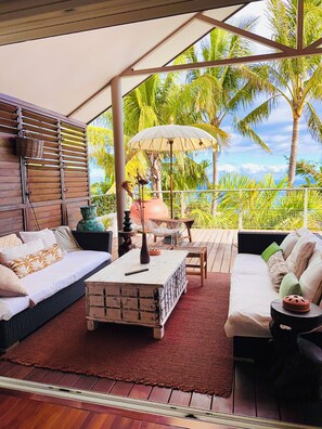 A covered outdoor seating area with a sofa, a coffee table, and a dining table.