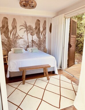 A bedroom with a bed, a bench, a wall mural, and a door leading outside.