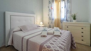 A neatly made bed with a patterned bedspread and pillows, a bedside table with a lamp, a dresser, and a window with curtains. - Villa Madrid Alcazar El Gastor by Ruralidays (Cádiz)