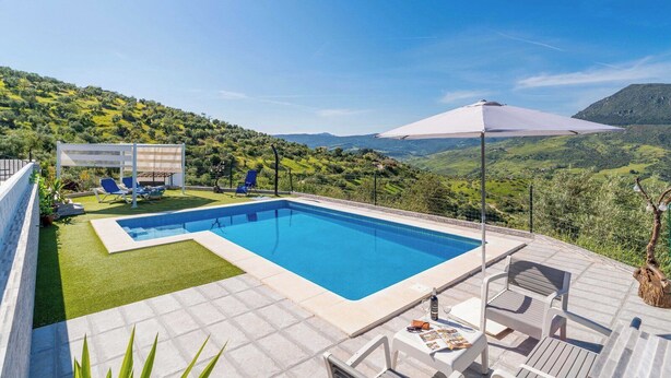 A rectangular swimming pool with a tiled deck, surrounded by a white fence and blue lounge chairs. - Villa Madrid Alcazar El Gastor by Ruralidays (Cádiz)