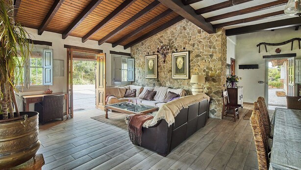 A cozy living room with a stone wall, wooden beams, and a large sofa.