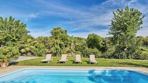 A swimming pool with four lounge chairs and a well-maintained garden.