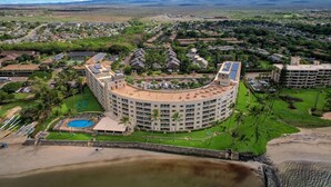 A large, circular hotel with multiple floors, a swimming pool, and a beach area. - Amazing Oceanfront Views! MS420 (Kihei)