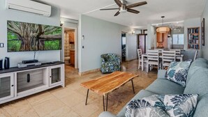 A spacious living area with a sofa, coffee table, TV, and a dining area with a table and chairs. - Amazing Oceanfront Views! MS420 (Kihei)