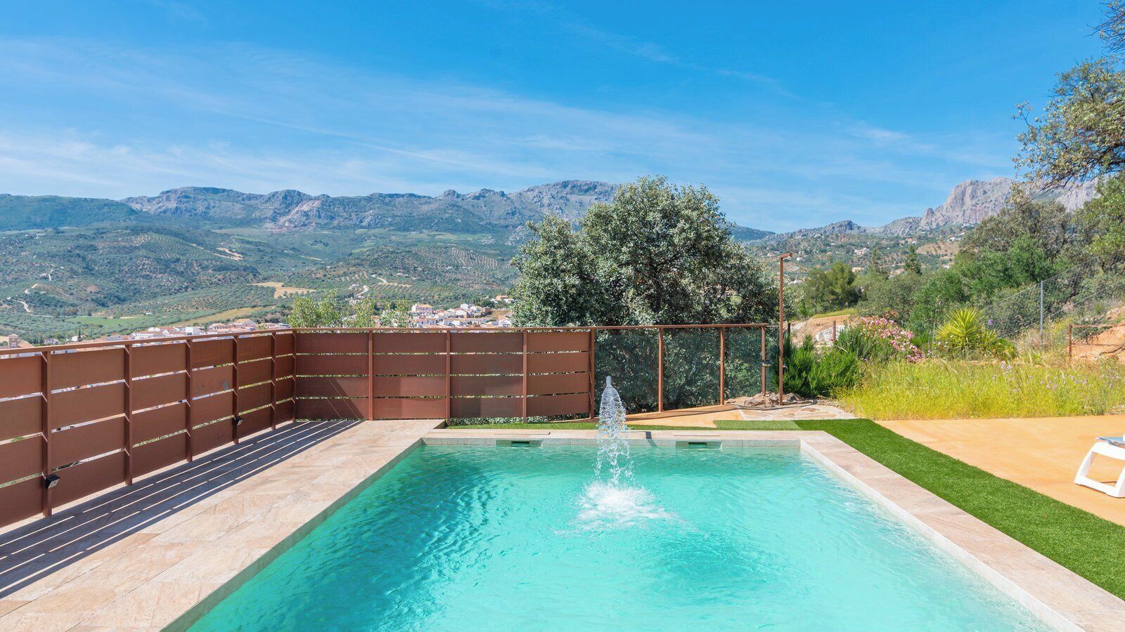 A rectangular swimming pool with a fountain, surrounded by a wooden fence and a grassy area.