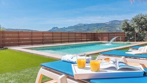 A poolside area with a view of mountains, a wooden fence, and a lounge chair with a book and glasses. - Villa Los Ruedos Riogordo by Ruralidays (Málaga)