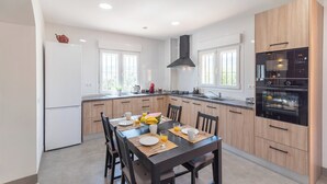A modern kitchen with wooden cabinets, a built-in oven, and a dining area with a table set for breakfast. - Villa Los Ruedos Riogordo by Ruralidays (Málaga)