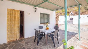 Un espace extérieur abrité, aménagé pour les repas, avec un sol en pierre, une table dressée pour deux personnes et une fenêtre ornée de volets verts.