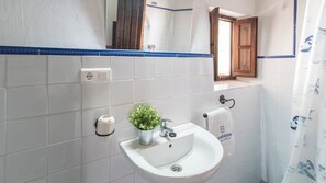 Une salle de bain avec un lavabo blanc, une petite plante en pot, un porte-serviettes et un miroir.