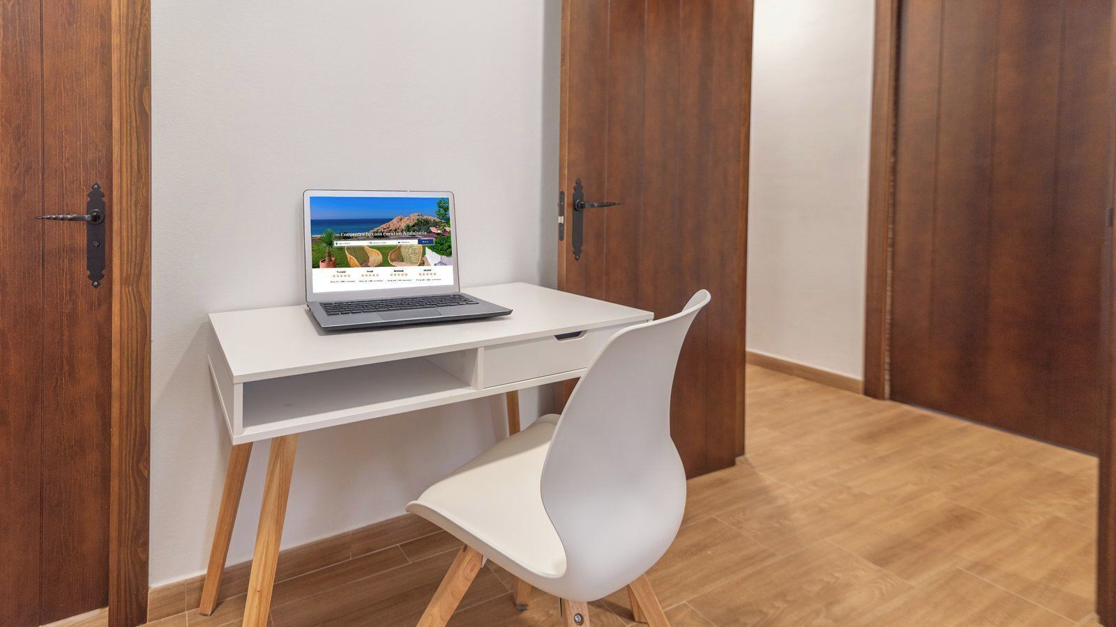 A room with a wooden door, a white desk with a laptop, and a white chair.