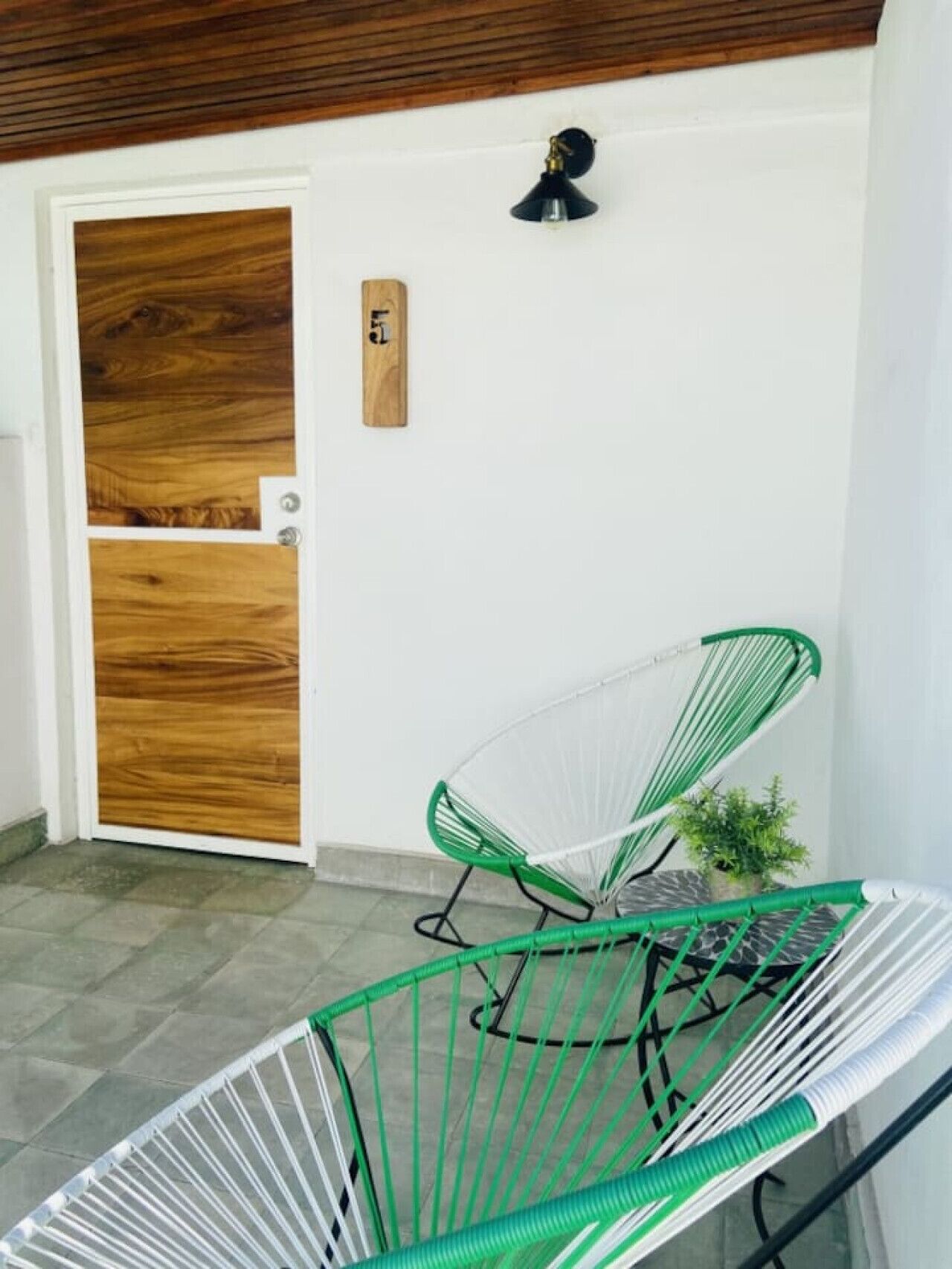 A room with a wooden door, a green chair, a small plant, and a wall-mounted light fixture.