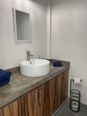 A bathroom with a white sink, wooden cabinets, a mirror, and a towel rack. - La paz Apartments (La Paz)