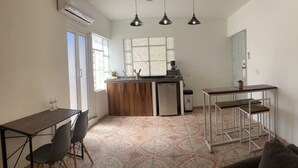 Cocina compacta con encimera de madera, un refrigerador pequeño y una cafetera. Hay una mesa de comedor con sillas y un sofá en la sala.