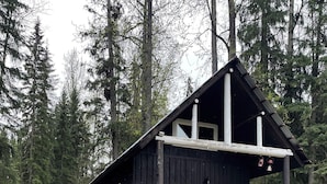A cabin with a porch, surrounded by trees and a grassy area with rocks. - Beaverfoot Lodge (Golden)
