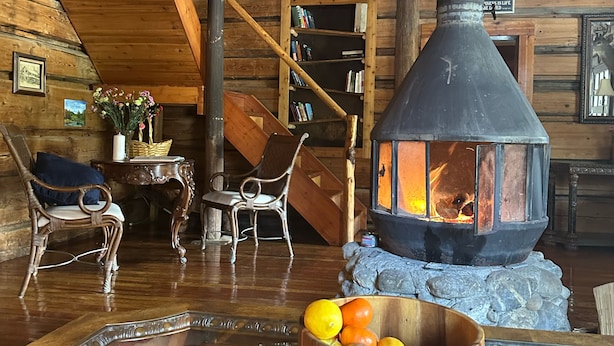 A cozy cabin interior with a wood-burning stove, rustic furniture, and a stone fireplace. - Beaverfoot Lodge (Golden)