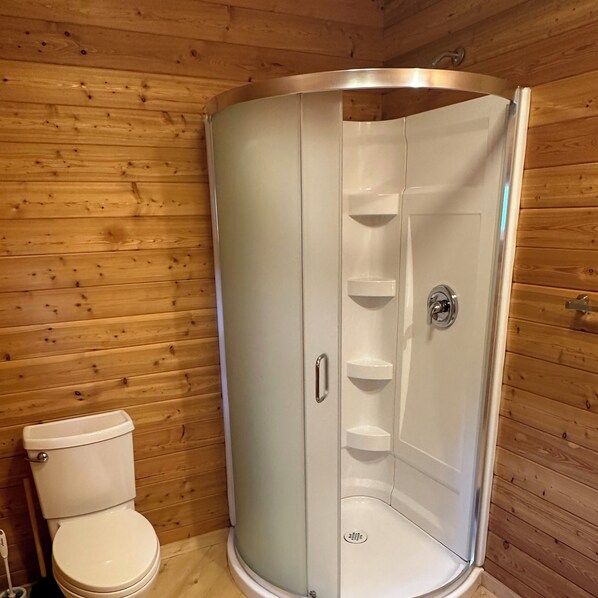 A wooden cabin bathroom with a white toilet, a shower stall, and a sink. - Beaverfoot Lodge (Golden)