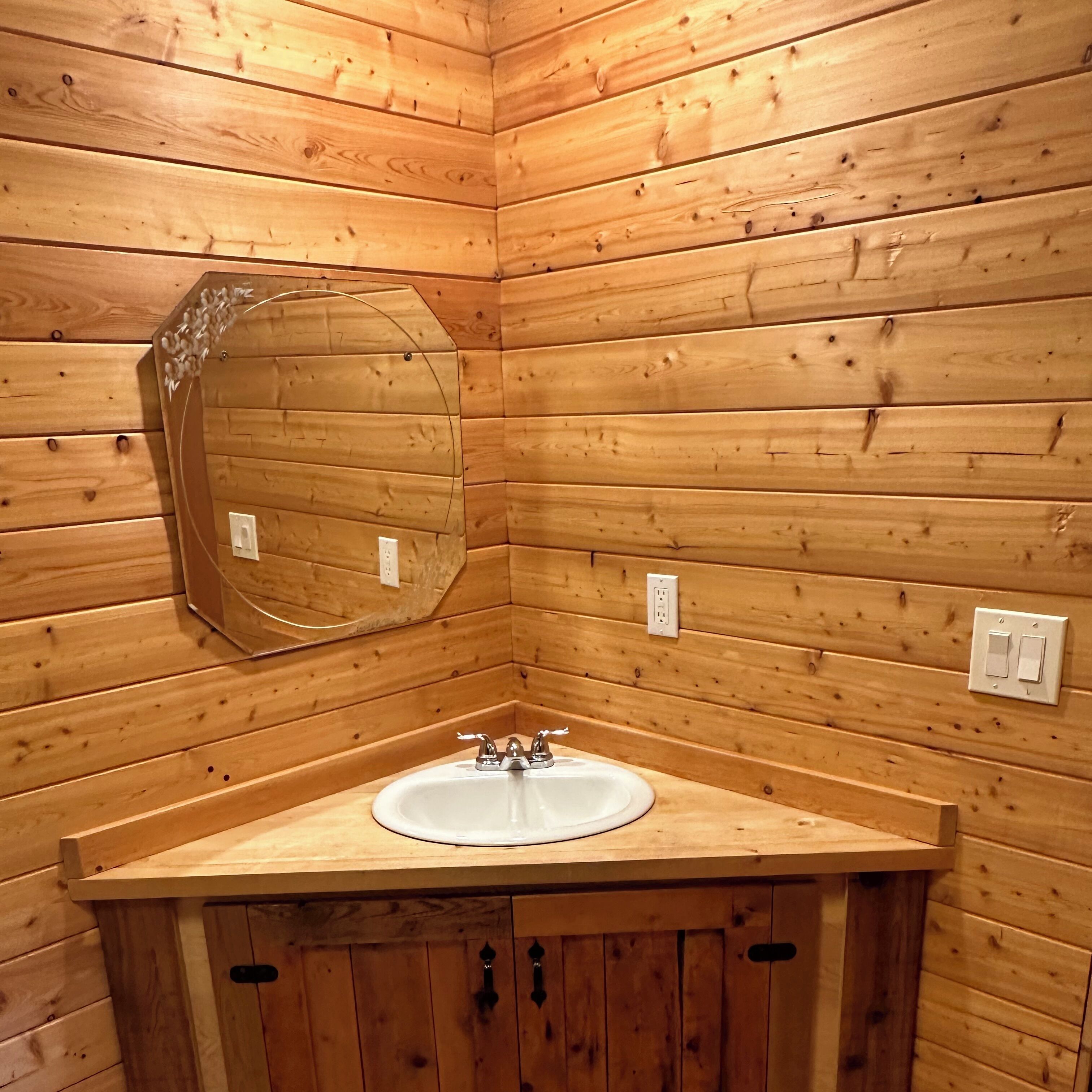 Un bagno in una casetta di legno con uno specchio rotondo, un lavandino e due interruttori a muro.