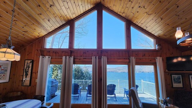 Een chalet met een groot erkerraam, houten inrichting en uitzicht op het meer.