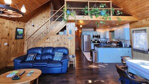 Een gezellig interieur van een blokhut met een houten trap, een zithoek met een blauwe bank, een keuken en een eethoek.