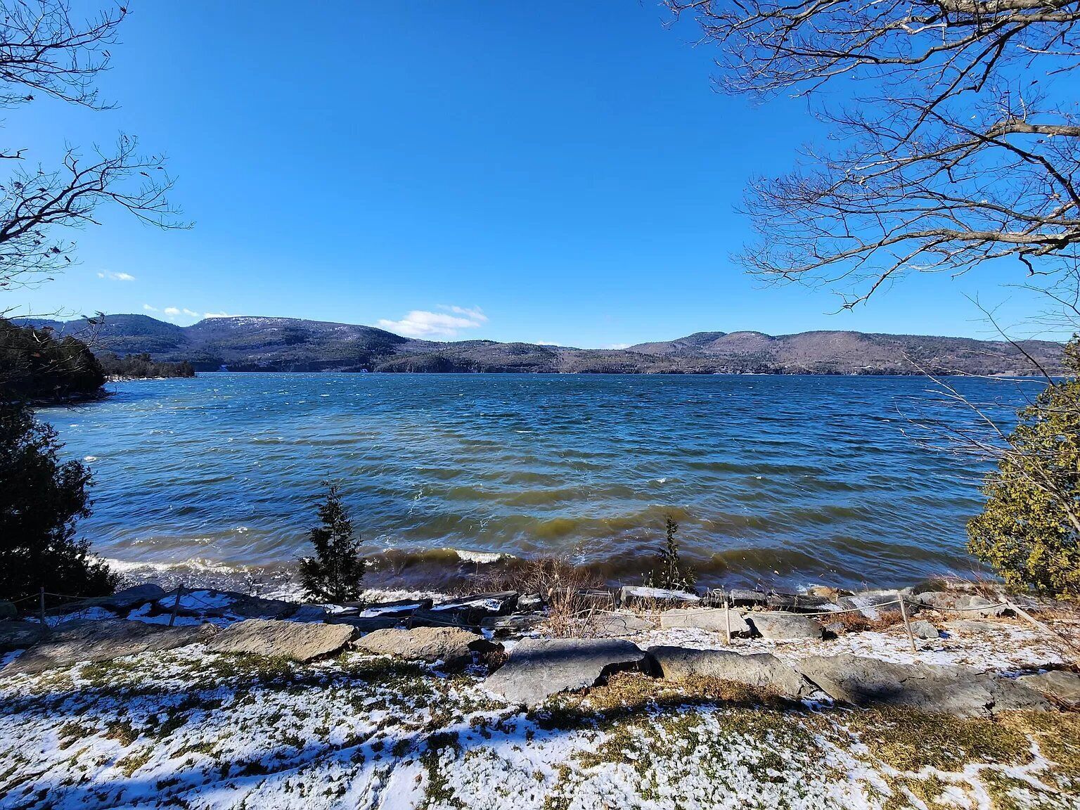 A lake with a rocky shoreline and snow patches.